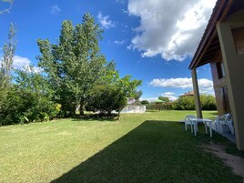 A backyard with a pool, a covered patio area, and a large tree.