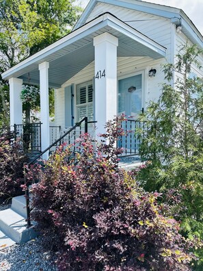 A white house with a porch, a number 414 sign, and a staircase leading to the entrance. - Quaint and charming 2 bed cottage with a putting green & outdoor shower! (Pensacola)