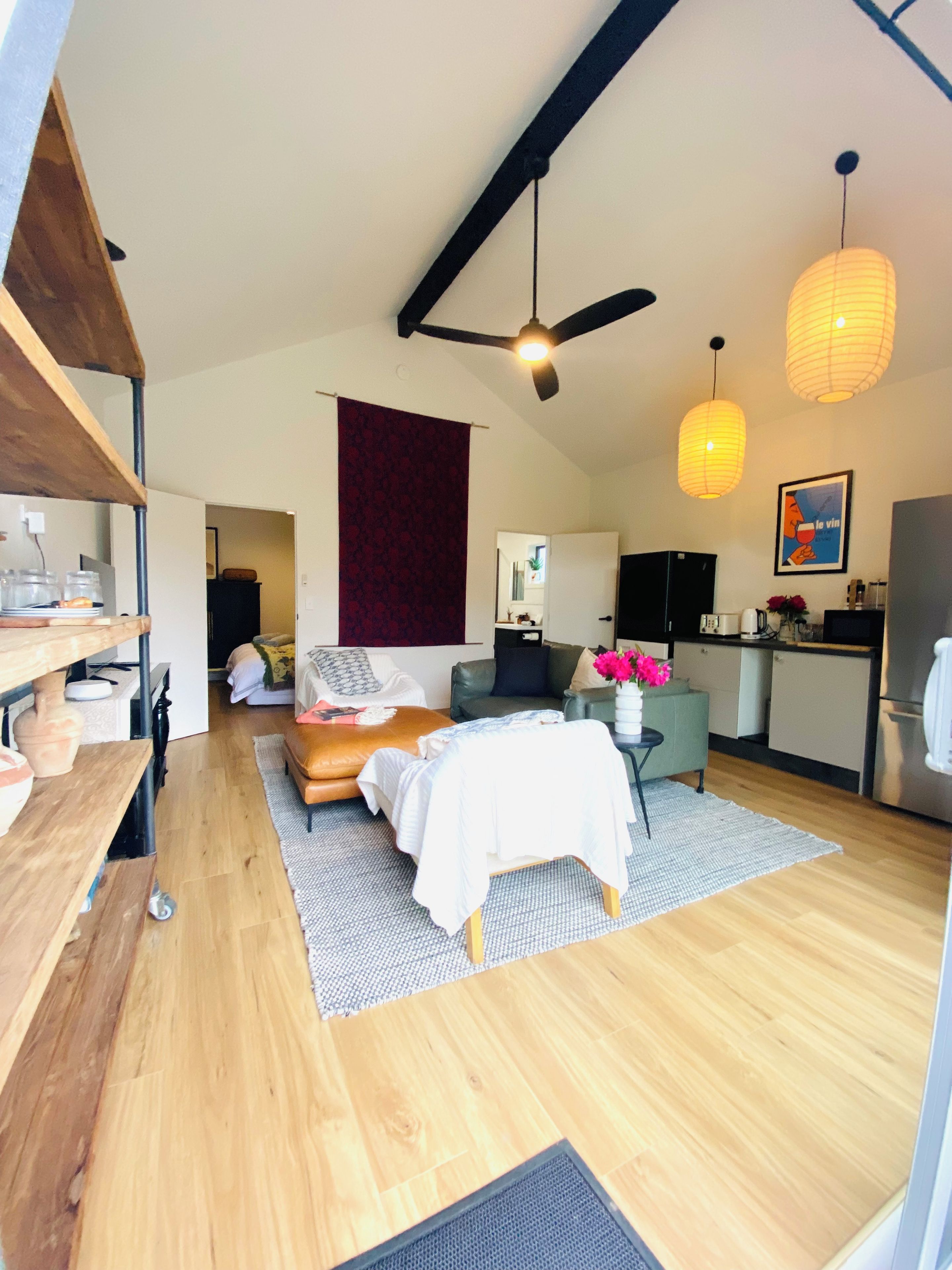 A modern living space with a bed, seating area, kitchen, and a ceiling fan.