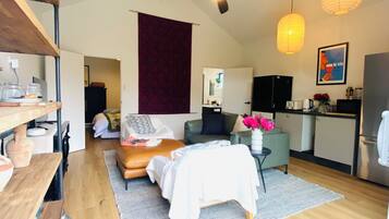 A modern living space with a bed, seating area, kitchen, and a ceiling fan.