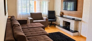 Een woonkamer met een bank, fauteuil en een open haard.