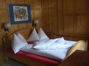 A wooden bed with white bedding, two wall-mounted lamps, and a framed picture on the wall. - Haus alte Post, (Samnaun-Compatsch) by Interhome (Samnaun)