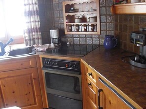 A kitchen with wooden cabinets, a built-in oven, a coffee maker, and a shelf with cups. - Haus alte Post, (Samnaun-Compatsch) by Interhome (Samnaun)