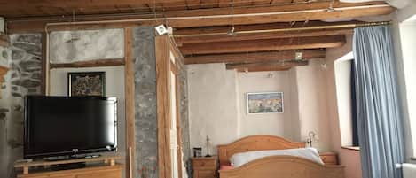 A bedroom with a wooden ceiling, a bed, a TV on a wooden dresser, and a stone wall.