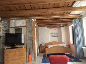A bedroom with a wooden ceiling, a bed, a TV on a wooden dresser, and a stone wall. - Haus alte Post, (Samnaun-Compatsch) by Interhome (Samnaun)