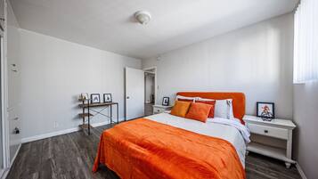 Un dormitorio con cama, mesita de noche, escritorio y puerta.