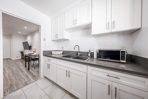 A modern kitchen with white cabinets, a black countertop, a sink, and a microwave. - Beverly Hills 1BR Sleeps 4, Parking, Near Cedars (Beverly Hills)