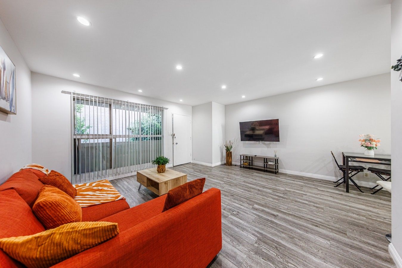 Uma sala de estar moderna com sofá, mesa de centro, televisão na parede e área de jantar com mesa e cadeiras.