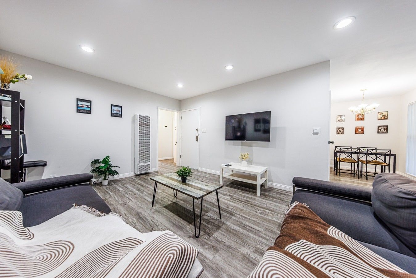 Uma sala de estar moderna com uma TV de tela plana, uma área de refeições com mesa e cadeiras e um corredor que dá para outro quarto.