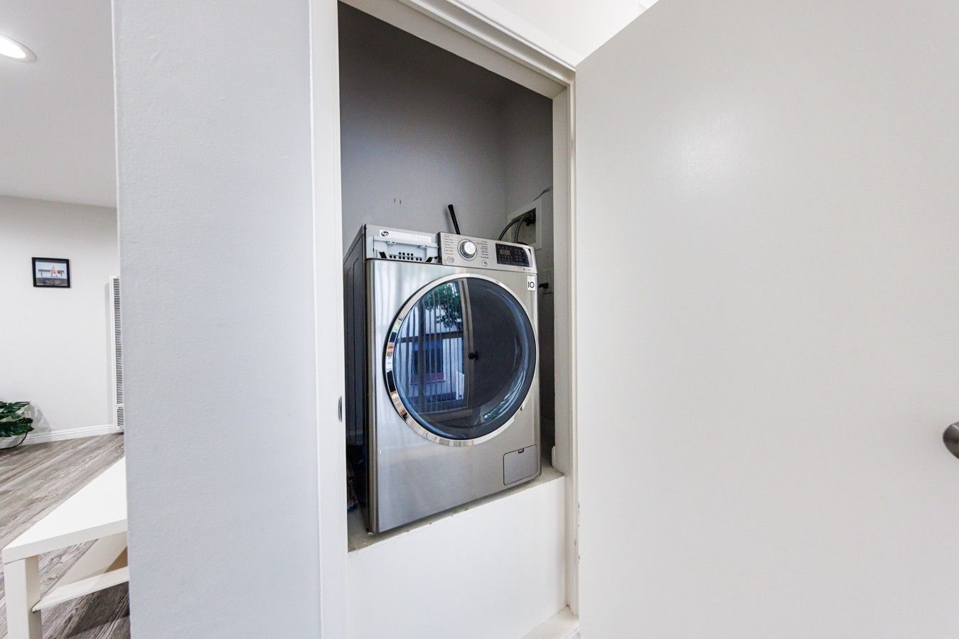 Una lavadora compacta de carga frontal integrada en un pequeño cuarto de lavado con una puerta blanca y piso de madera.