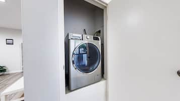 Una lavadora compacta de carga frontal integrada en un pequeño cuarto de lavado con una puerta blanca y piso de madera.