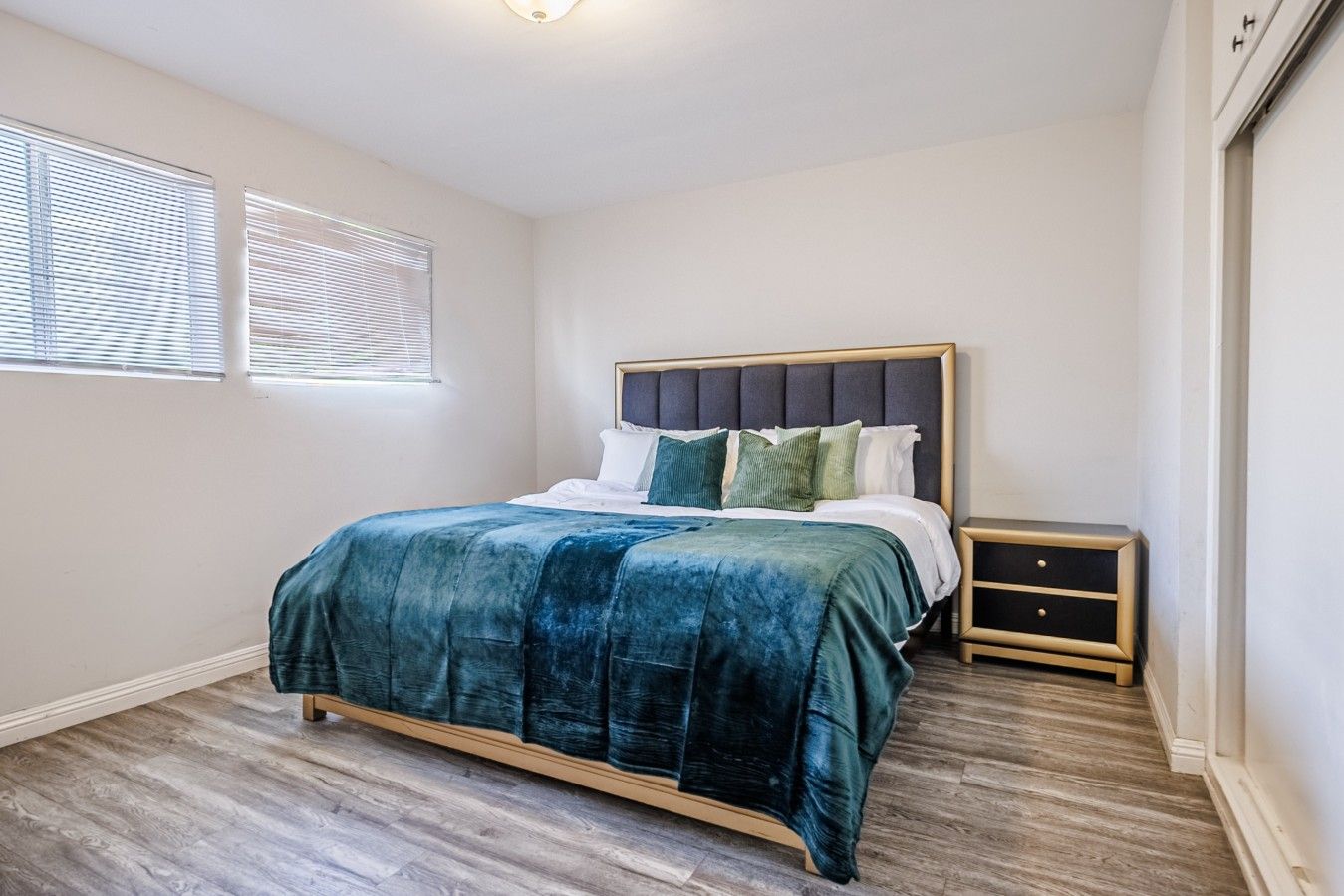 Quarto com cama, mesas de cabeceira e janela com persianas.