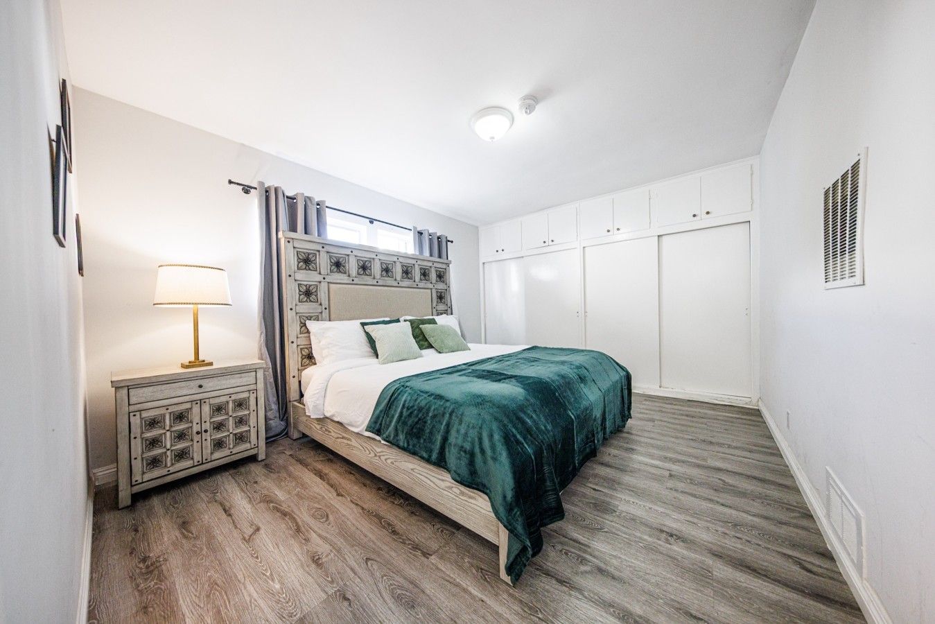 Une chambre à coucher comprenant un lit, une table de chevet, une lampe, des rideaux et une armoire.