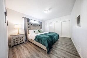 Ett sovrum med en säng, ett sängbord, en lampa, gardiner och en garderob.
