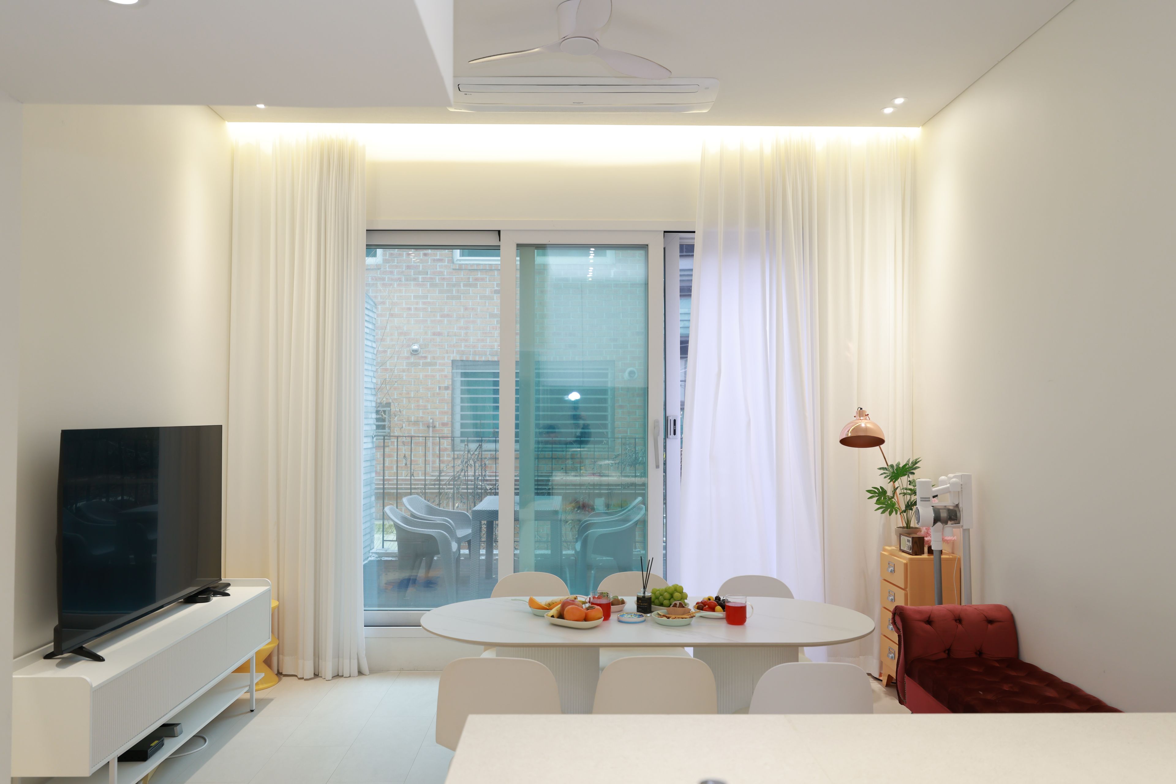 Una sala moderna con televisor de pantalla plana, una mesa de comedor con sillas, un sofá rojo y un ventanal con cortinas.