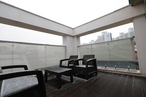 A rooftop terrace with a seating area, a view of the cityscape, and a glass balustrade.