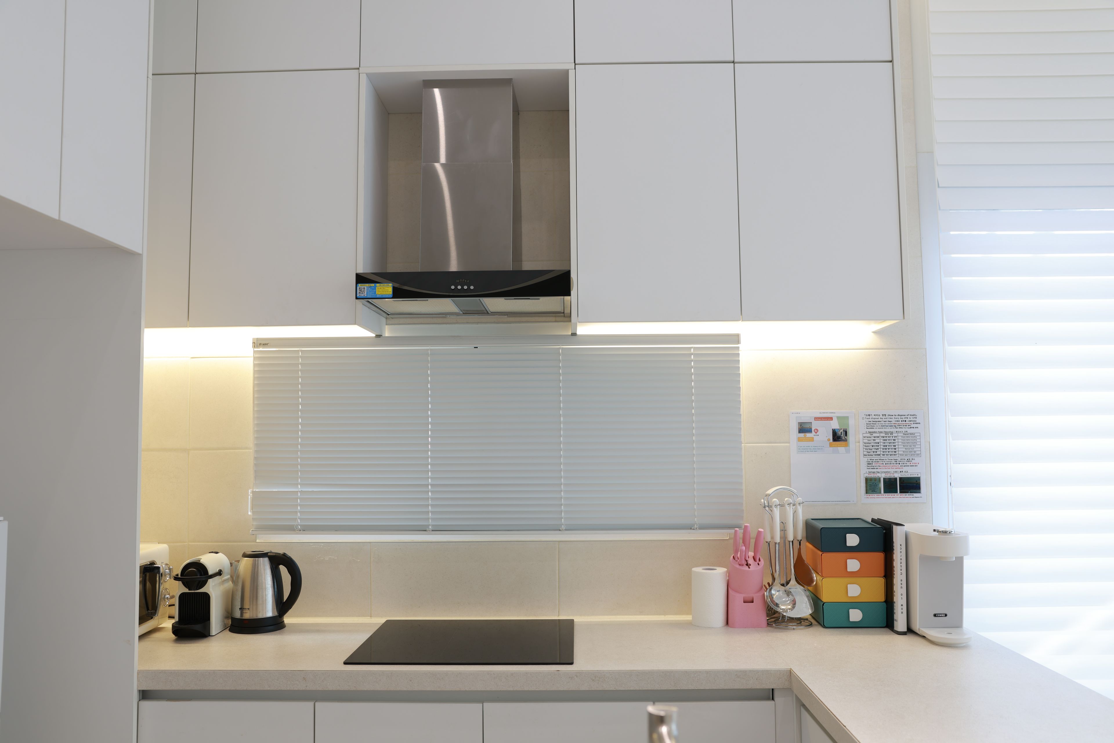 A modern kitchen with white cabinets, a stainless steel range hood, a kettle, and a coffee maker.
