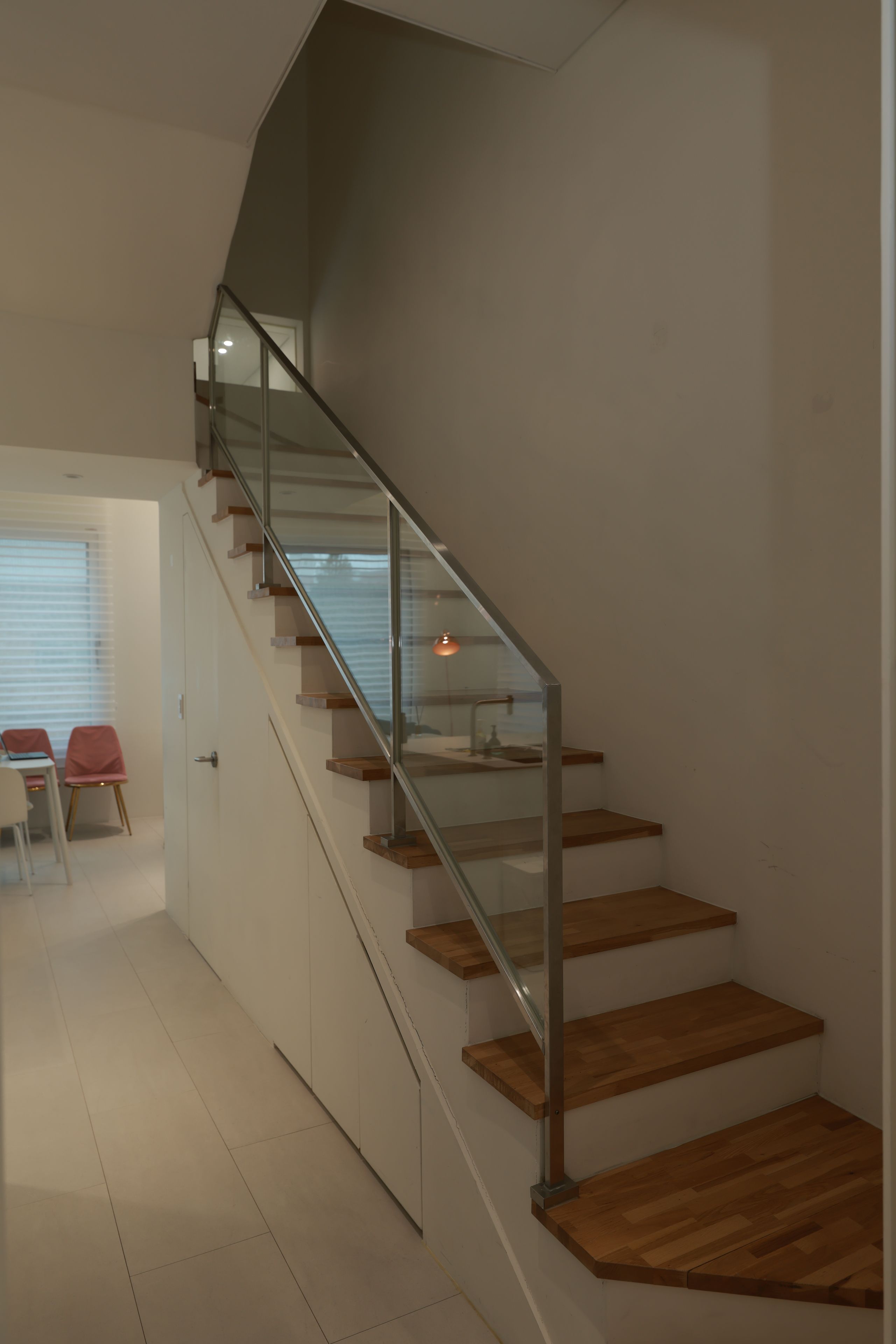 A modern staircase with glass railings and wooden steps, leading to a room with a dining area.