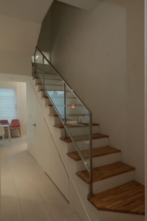 A modern staircase with glass railings and wooden steps, leading to a room with a dining area. - Seocho/Gangnam - Charming Family Home - 3-Story-Home - 15 Guests - 3BR/3BTH (Seoul)