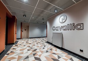 Ein Flur mit einem geometrisch gemusterten Boden, einem an der Wand befestigten Schild mit der Aufschrift 'cavallia' und einer Tür mit der Bezeichnung '58'.