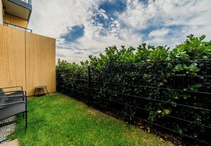A modern outdoor area with a wooden wall, a metal fence, and green plants. - Kawaleryjska Homely Apartment (Poznań)