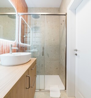 Un bagno moderno con cabina doccia in vetro, lavandino bianco e mobile bagno in legno.