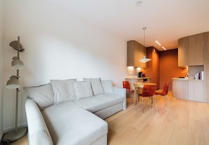Un soggiorno moderno con un divano componibile, una zona pranzo con tavolo e sedie e una cucina con mobili in legno.