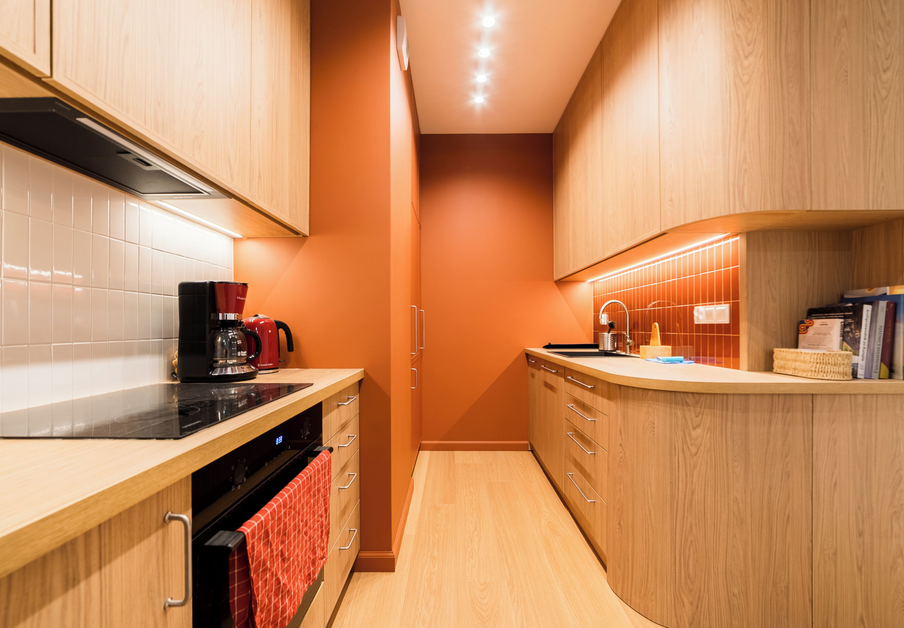 A modern kitchen with wooden cabinets, a black stove, and a red kettle.