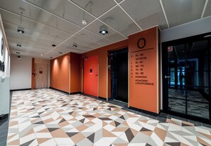 A hallway with geometric patterned flooring, a fire exit sign, and a directory on the wall. - Kawaleryjska Homely Apartment (Poznań)