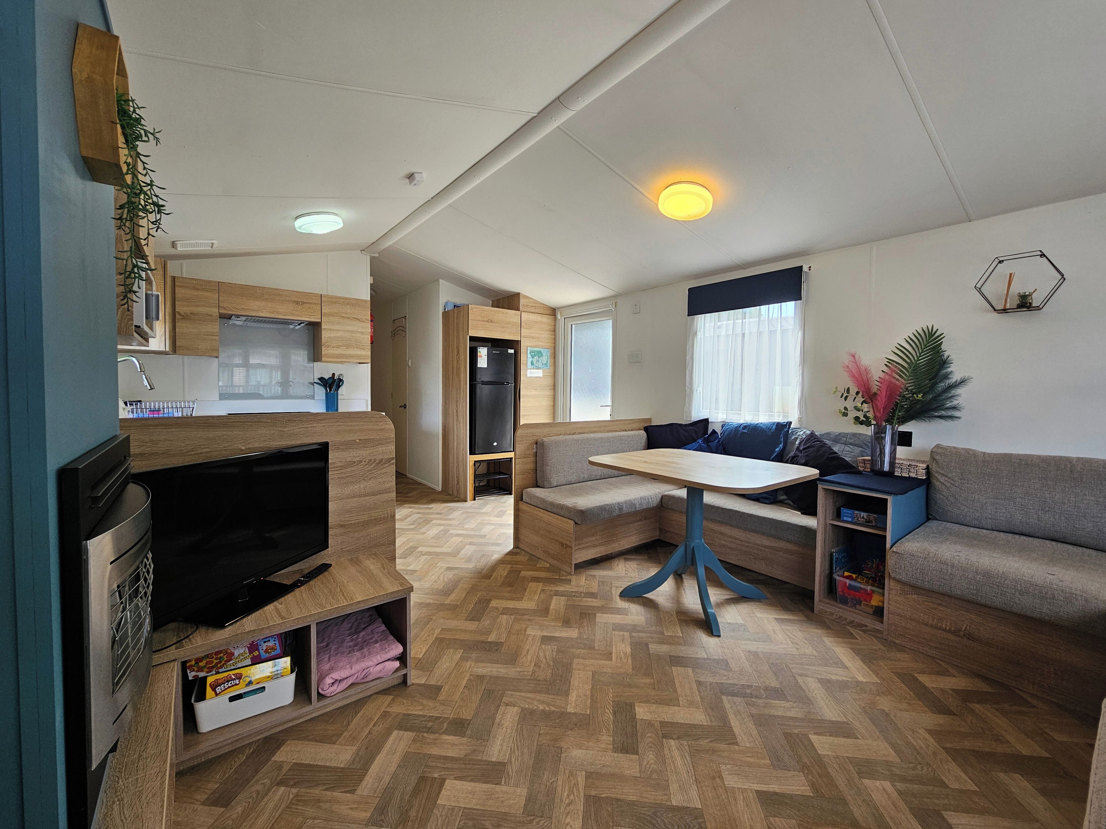A compact living space with a kitchenette, a sofa, a small table, and a television.