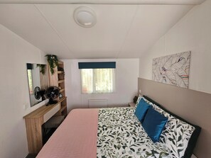 Une chambre à coucher avec un lit, une commode, un miroir, une fenêtre et un radiateur.