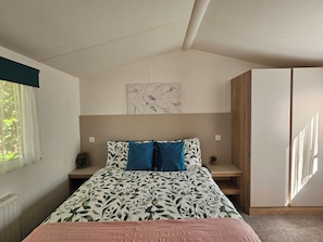 Een slaapkamer met een bed, een raam, een radiator, een aan de muur hangend kunstwerk en een houten garderobe.