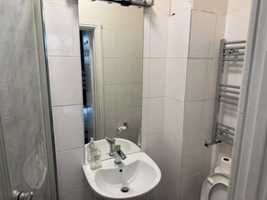 Ein Badezimmer mit weißem Waschbecken, Spiegel, Toilette und Duschbereich.