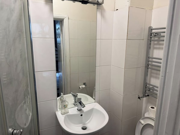 A bathroom with a white sink, a mirror, a toilet, and a shower area. - Ensuite Studio, Sleeps 4 with WiFi (London)