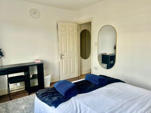 Een slaapkamer met een bed, een bureau, een stoel, een spiegel en een deur.