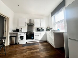 A modern kitchen with white cabinets, a built-in oven, a washing machine, and a window providing natural light. - Charming London Apartment with 2 Bedrooms (London)