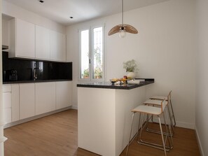 Une cuisine moderne avec des meubles blancs, un plan de travail noir et un petit îlot central doté de tabourets.