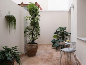 A small patio area with a herringbone floor, a tall potted plant, a metal chair, and a table with a glass container. - Hommyhome Felipe II - Sevilla (Sevilla)