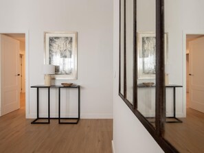 A hallway with a framed artwork on the wall, a small table with a lamp and a bowl, and a wooden floor. - Hommyhome Felipe II - Sevilla (Sevilla)