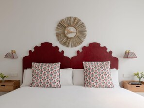 A bed with a red headboard, two patterned pillows, and a wall-mounted circular mirror. - Hommyhome Felipe II - Sevilla (Sevilla)