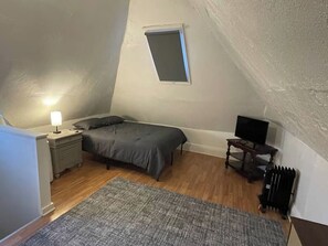 A bedroom with a bed, a nightstand, a lamp, a television, a radiator, and a window. - 2 Apts • 3 Private Parking Spaces • Near CMU/Pitt (Pittsburgh)
