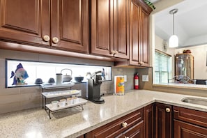 A kitchen with wooden cabinets, a coffee maker, a tea kettle, and a window with decorative items. - 4BR Pinellas Park Beach & Game Home (Pinellas Park)