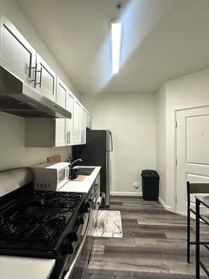 A compact kitchen with white cabinets, a black stove, a microwave, and a stainless steel refrigerator. - Cozy Austin Getaway - Game Room - Minutes to UT (Austin)