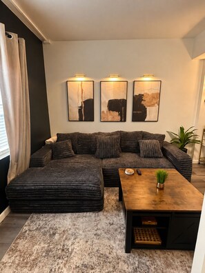 A modern living room with a sectional sofa, a coffee table, and three abstract paintings on the wall. - Cozy Austin Getaway - Game Room - Minutes to UT (Austin)