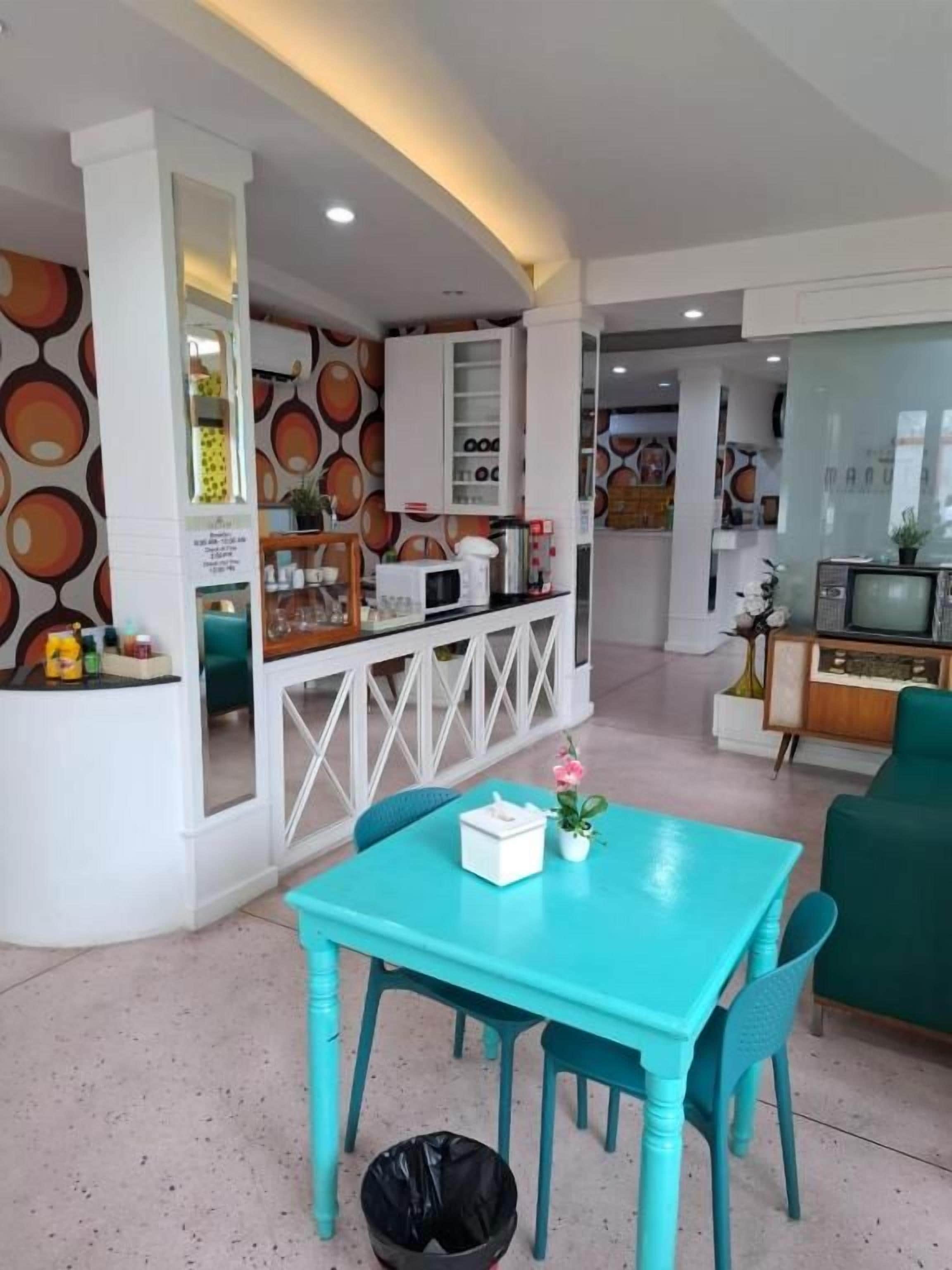 Un interior moderno con una mesa y sillas de comedor color turquesa, una zona de cocina con microondas y un televisor.