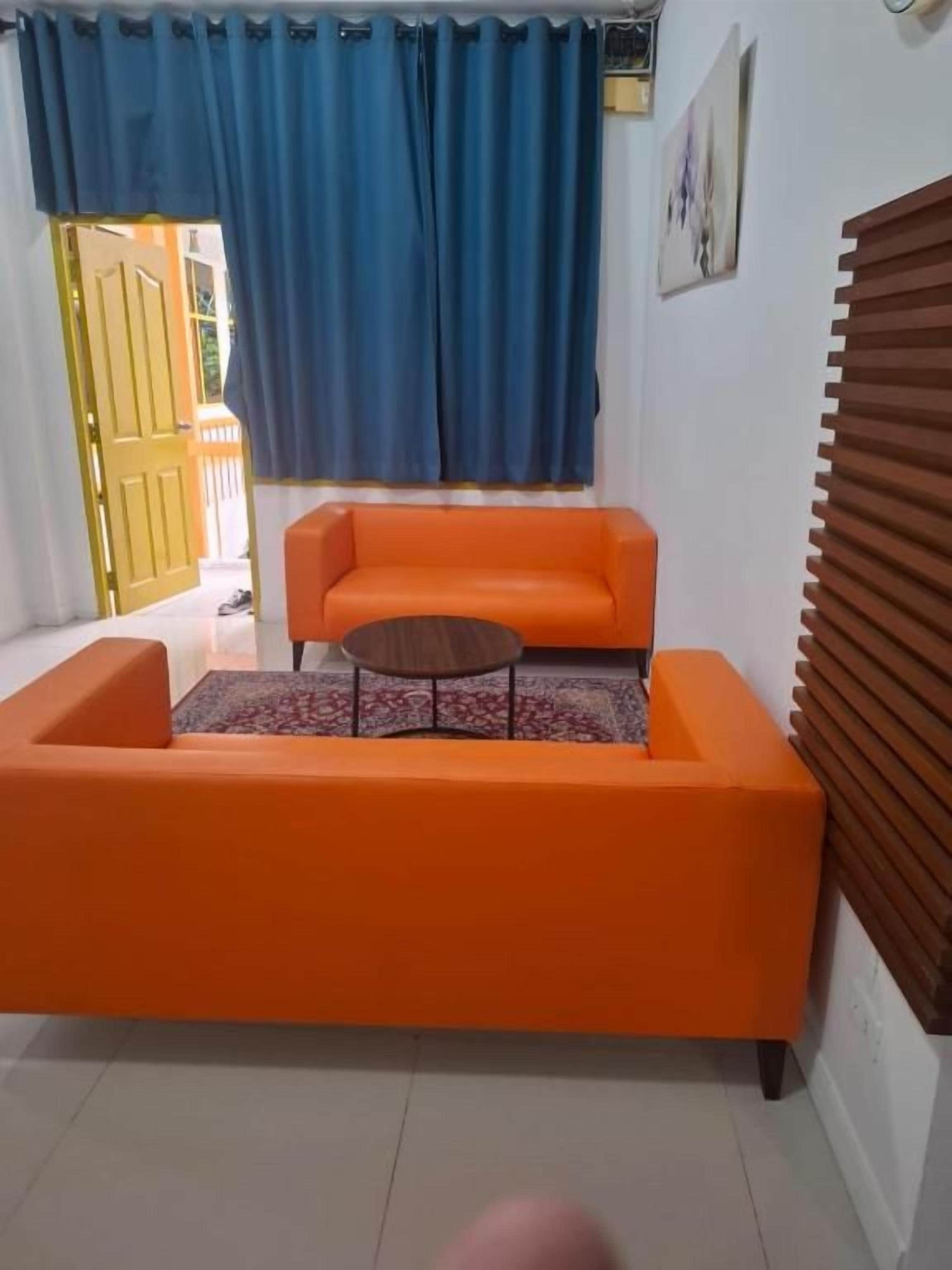 Une pièce avec un canapé orange, une petite table ronde et un rideau bleu.