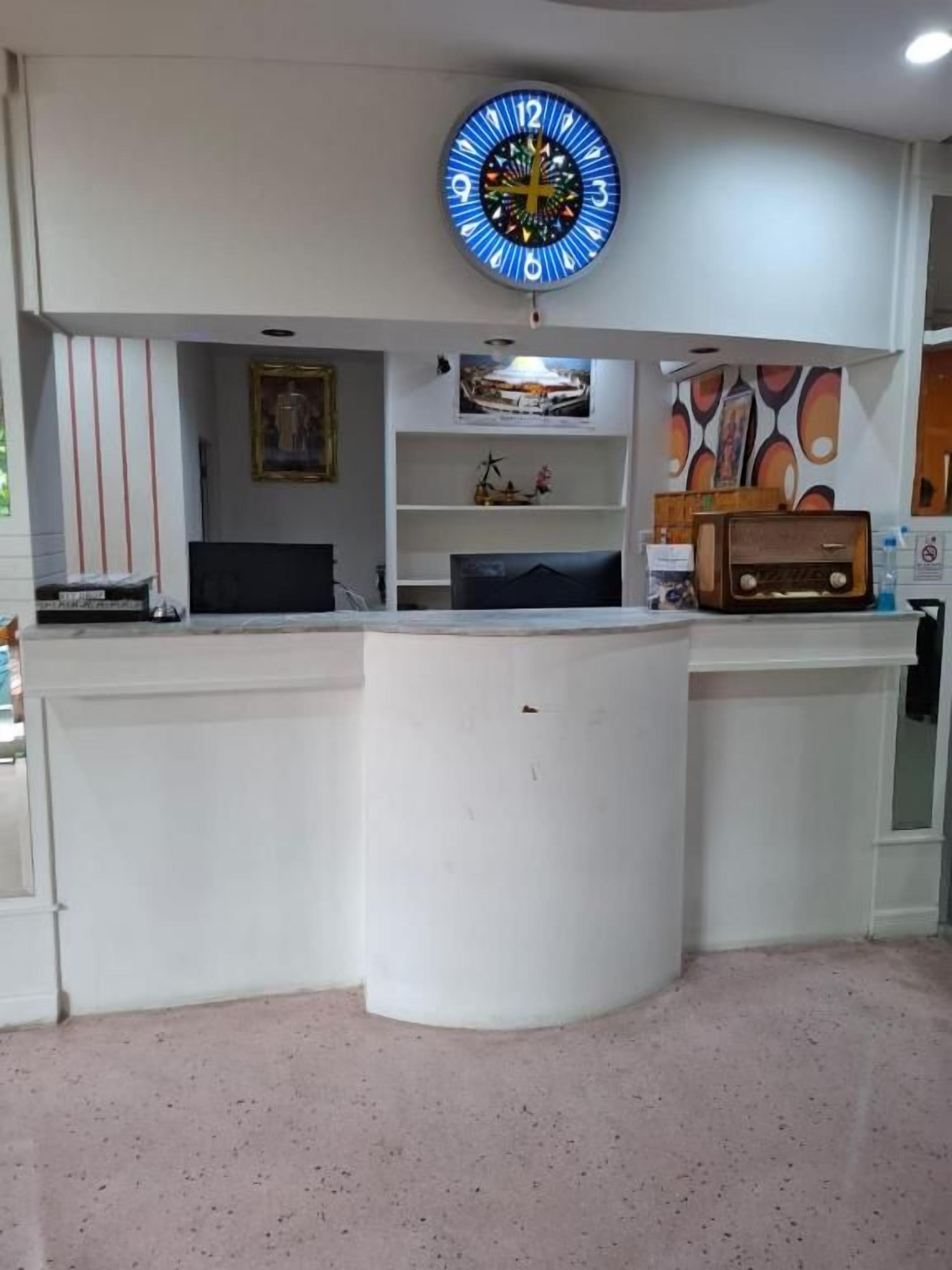 Un área de recepción con un mostrador blanco curvo, un reloj de pared grande y estantes con diversos objetos.