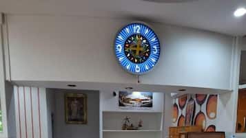 Un espace d’accueil doté d’un comptoir blanc incurvé, d’une grande horloge murale et d’étagères contenant divers objets.