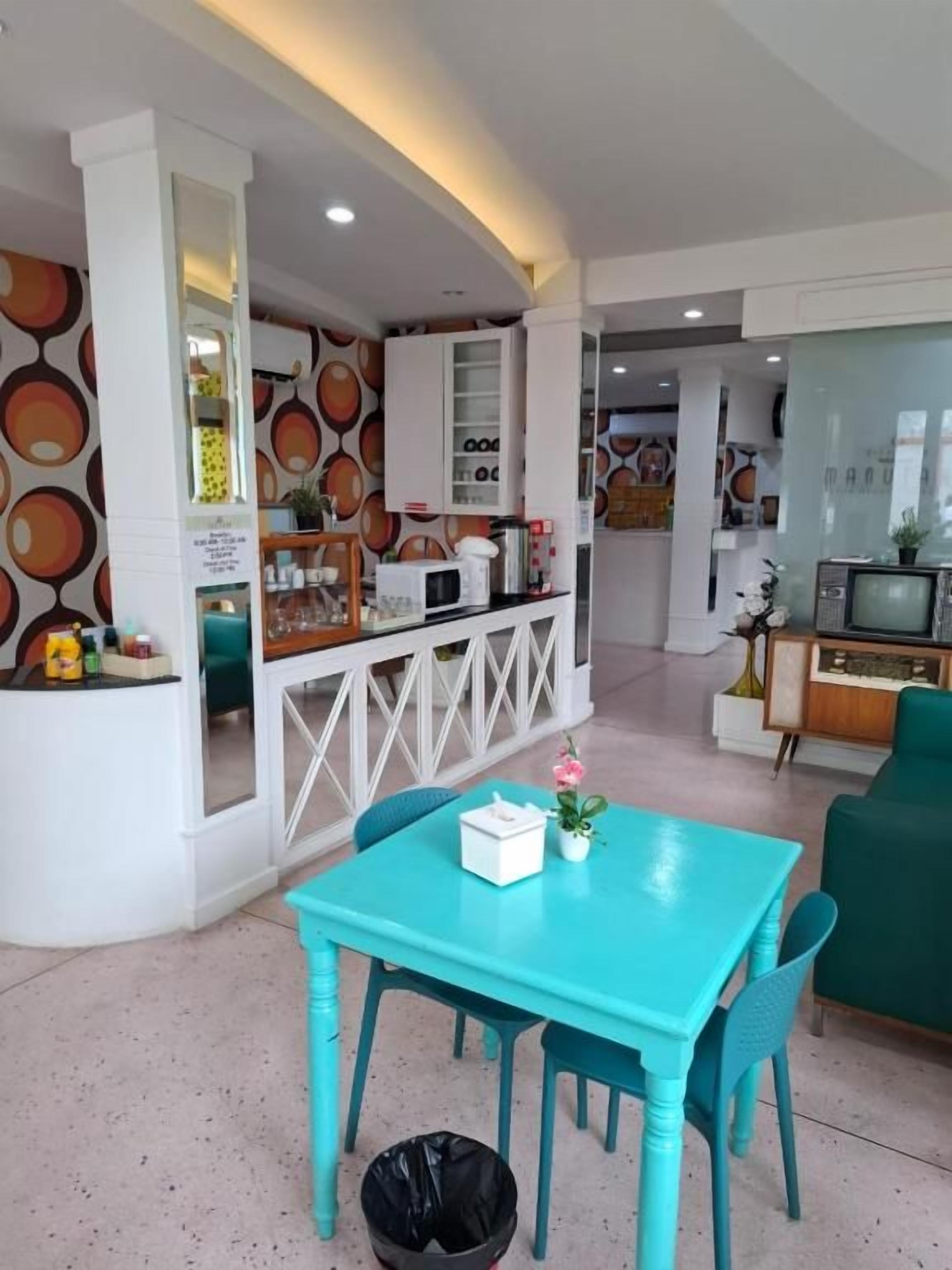 Un interior moderno con una mesa y sillas de comedor color turquesa, una zona de cocina con microondas y un televisor.