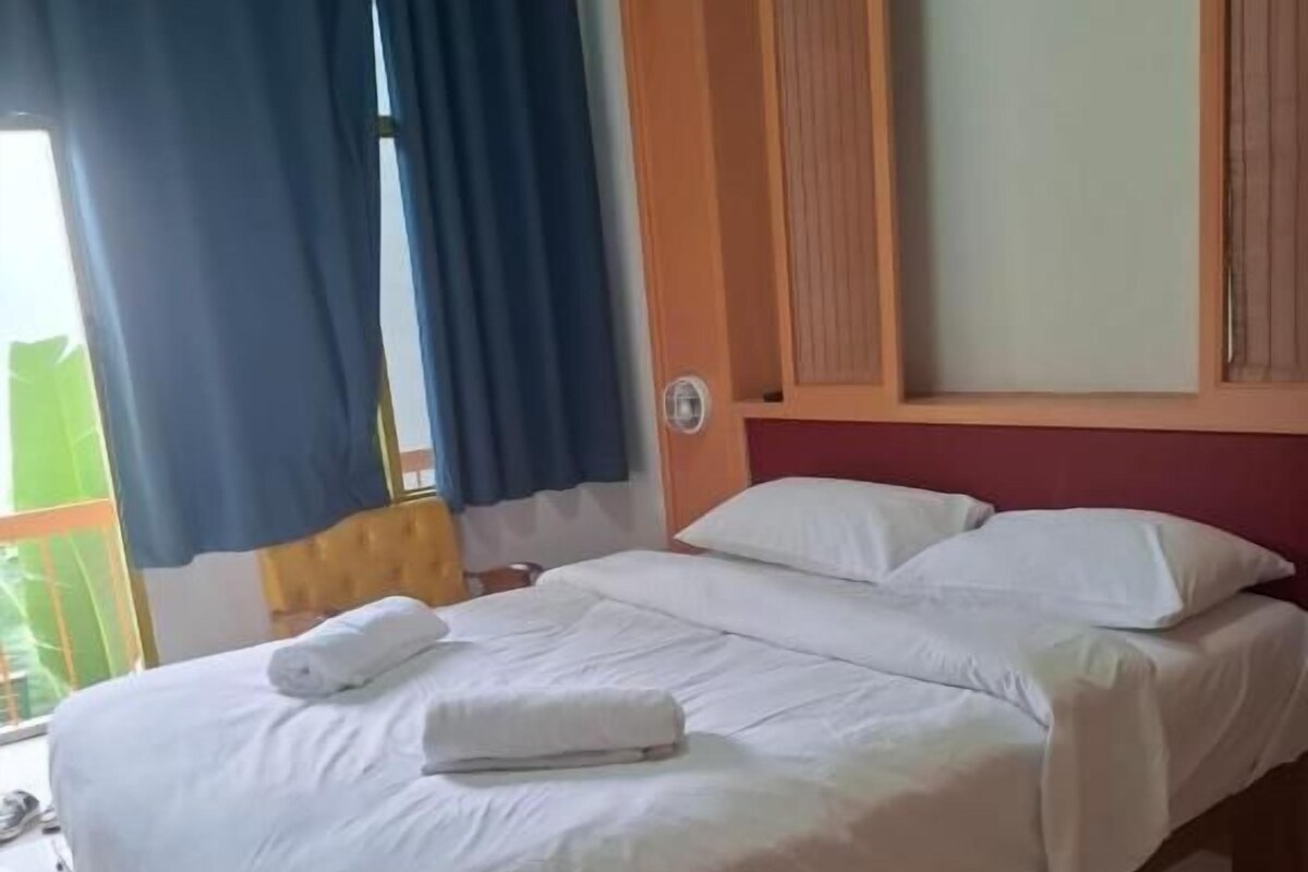 Habitación de hotel con cama, cortinas, cabecero de madera y vista al exterior.